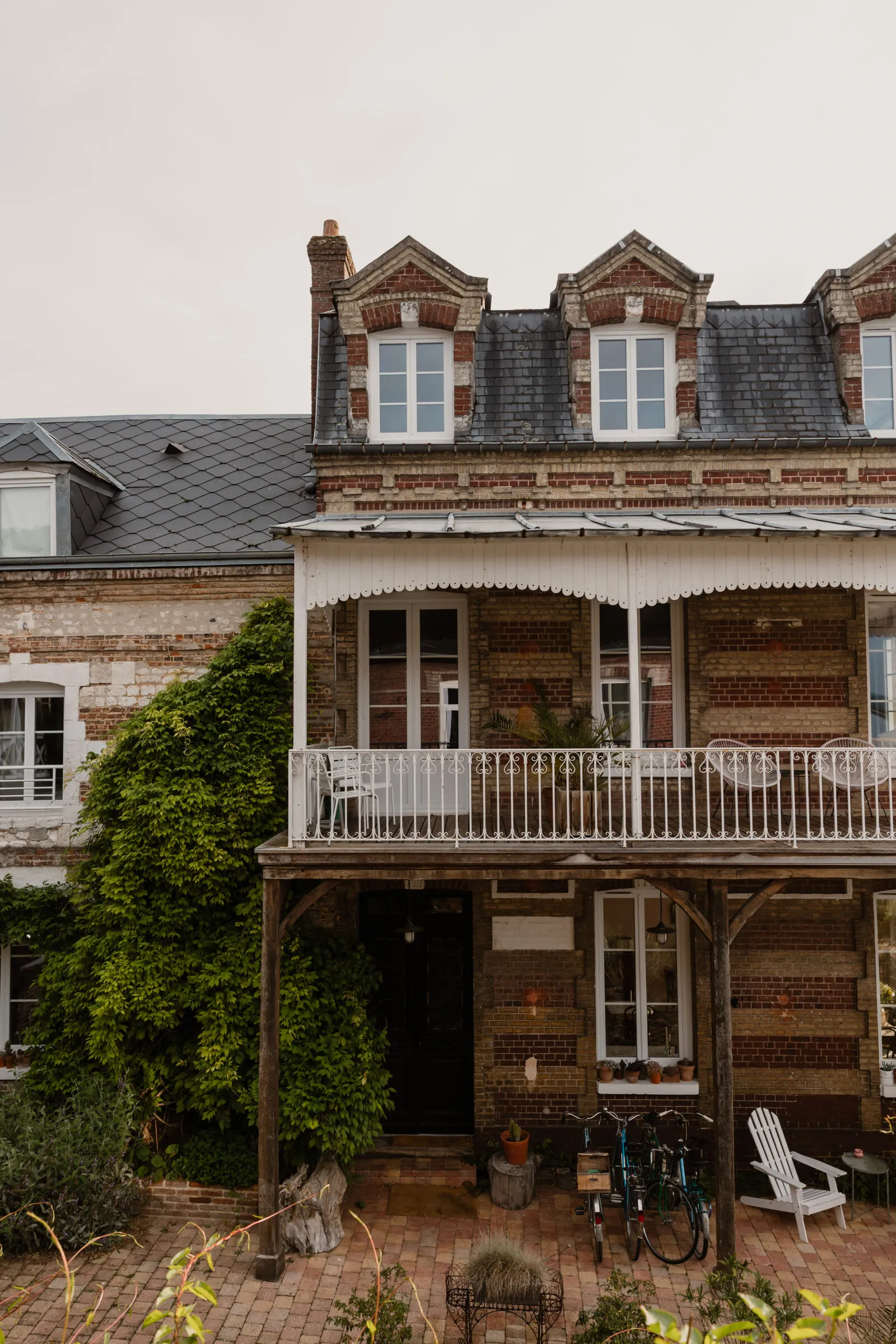 La façade en brique de la maison, son balcon de bois et son lierre